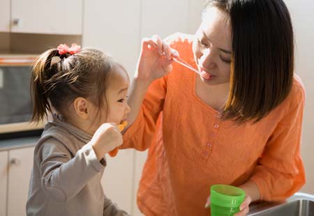 Mom teaching daughter how to brush her teeth