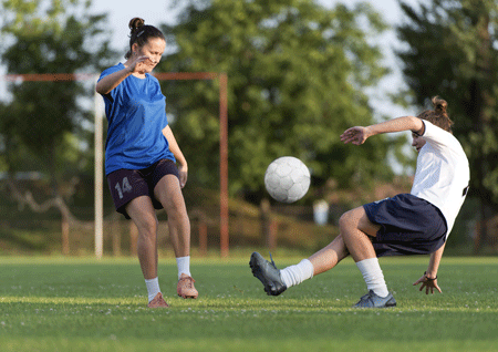 girls playing soccer on a field with one falling about to experience a scaphoid bone fracture