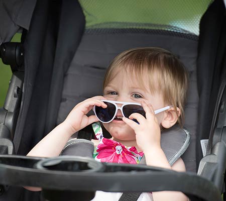 little girl peaks out from behind her sunglasses that are prevent eye problems caused by the sun