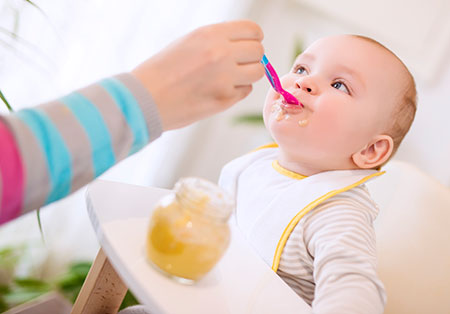 Mother feeding baby solid foods - Feeding babies peanut products reduces allergy risk