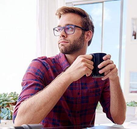 Young man drinking coffee wondering if he has one of the signs of testicular cancer after a self-exam