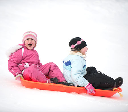 two kids sledding with parents concerned about windburn sunburn and snow