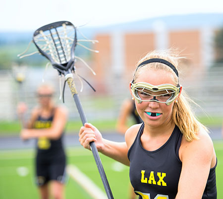 young woman playing lacrosse with mouth guard to prevent chipped teeth