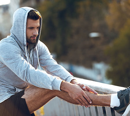 Man stretching his leg outside in a sweatshirt / treating shin splints