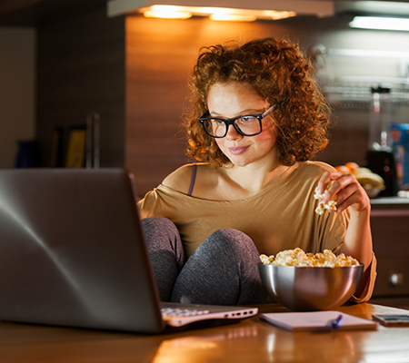 young woman eating popcorn watching a video on her laptop nighttime / curbing nighttime eating