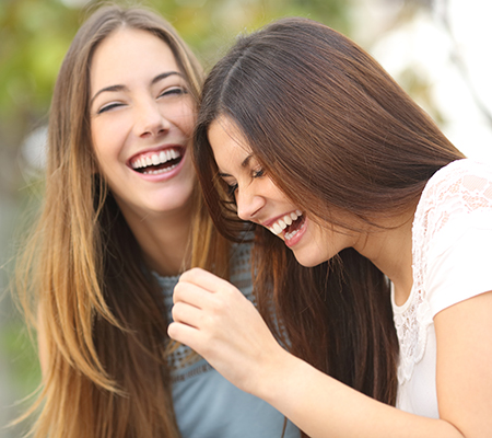 Two millennial women laughing - Benefits of laughter