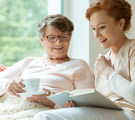 Senior woman and young woman enjoying a cup of tea and reading a book - What is palliative care?