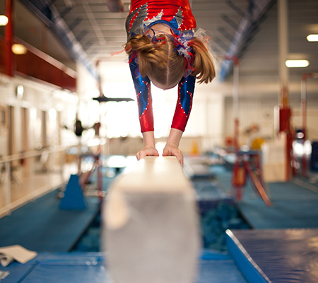 Girl balancing on a high beam on her hands - Gymnastics injuries