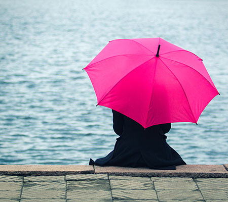 Woman sitting beside a lake with a pink umbrella - Is solitude healthy?