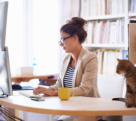 Woman typing at her desk with her cat nearby - Dead butt syndrome