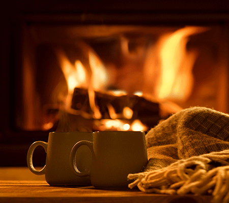 two mugs and a blanket in front of a fireplace / wood burning stoves and fireplaces