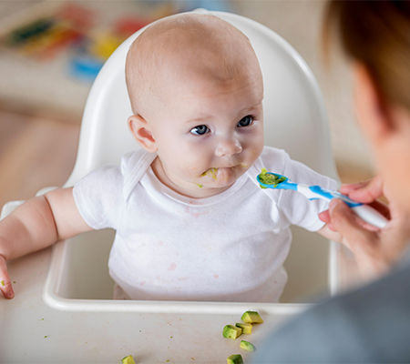 Baby eating avocado in a high chair - Tips for transitioning from baby food to solids