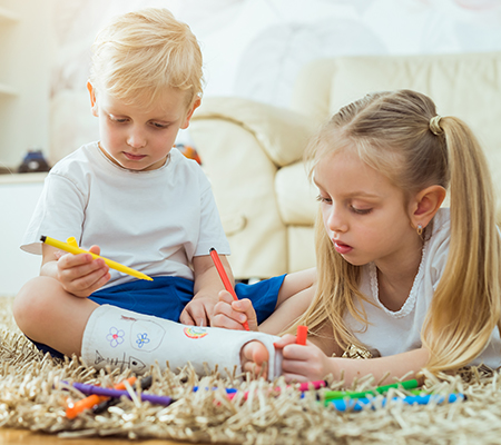 Two kids draw on a boy's waterpoof cast.