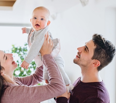 A portrait of young couple with a baby and cardboard boxes moving in a new home.