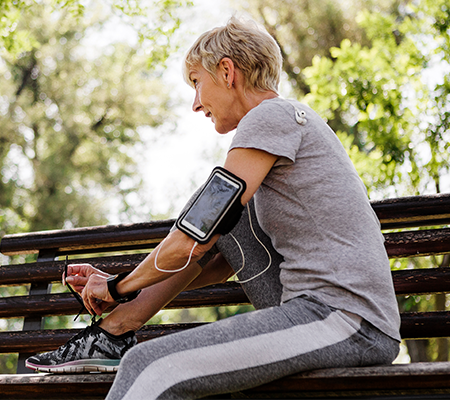 woman over 50 sitting on bench putting shoes on about to workout