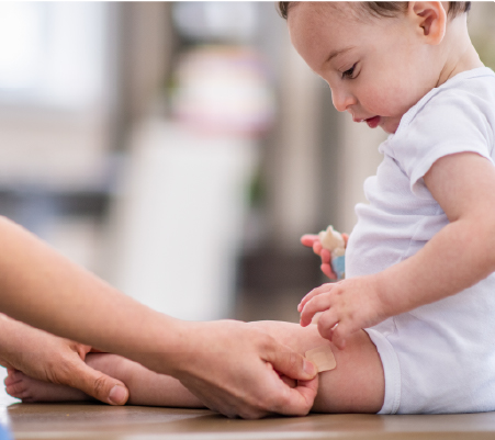 Infant getting band-aid placed on their leg by an adult after adhering to the childhood immunization schedule