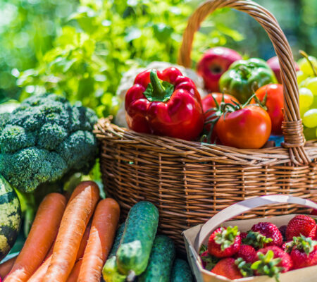 A photo of fresh fruit and vegetables in a basket surrounded by more fresh produce. 