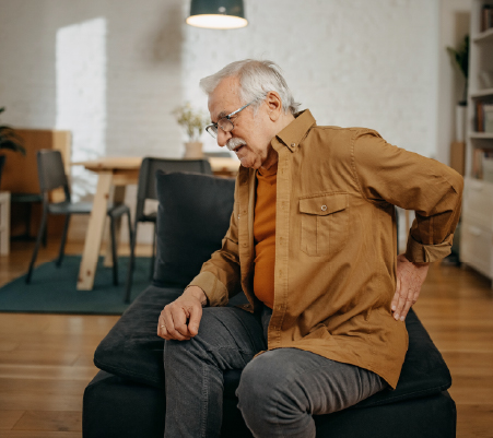 A man sitting on a chair with his hand on his back in pain.