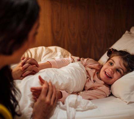parent talking to young girl laying in bed about bedwetting